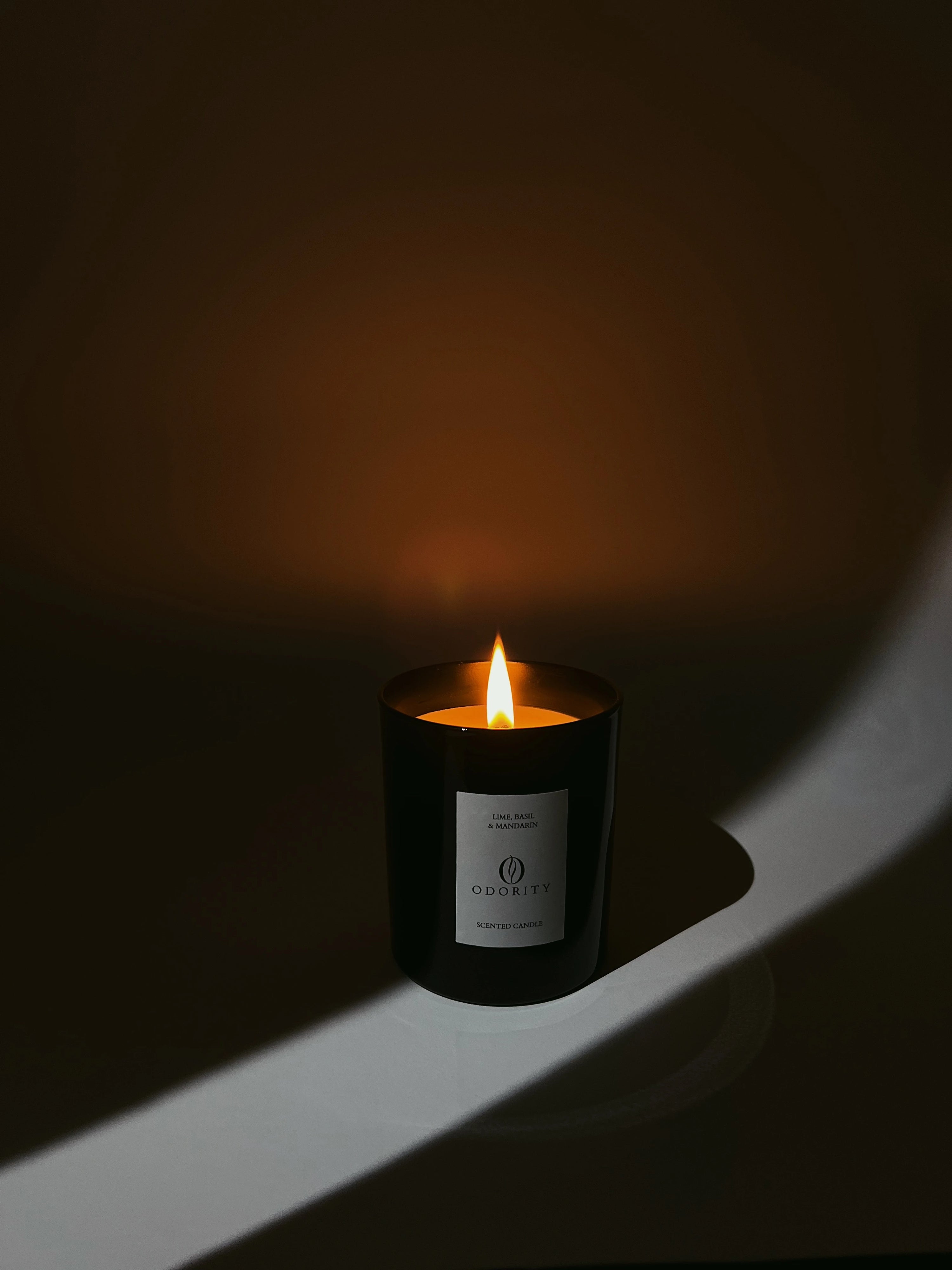 Rapswachs Duftkerze Lime, Basil & Mandarin in schwarz von Odority angezündet in einem Lichtspalt stehend.